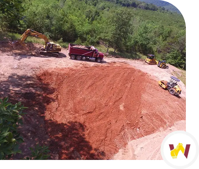 A large red dirt pile with several vehicles in the background.